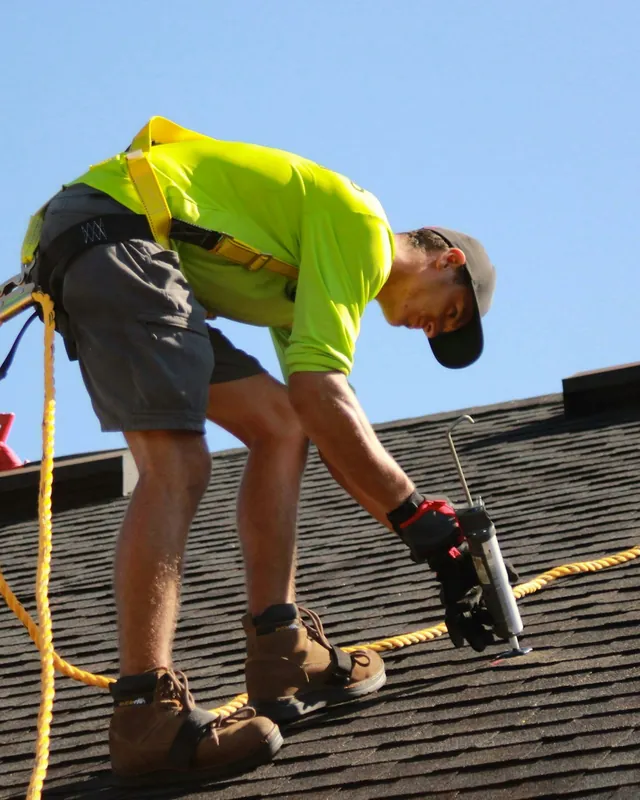 Roofer in a safety harness fastening shingles on a roof